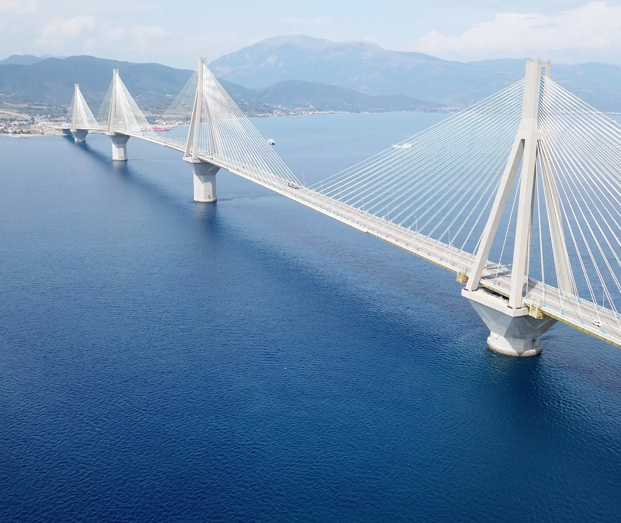 A cable-stayed bridge crossing open blue water toward the mountains