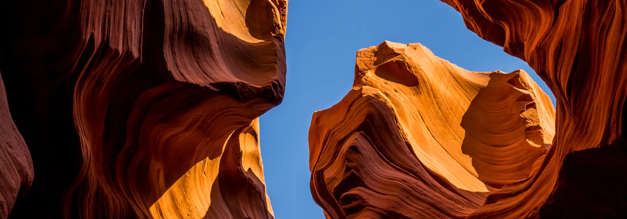 Looking up through the curved red sandstone walls of a slot canyon toward a blue sky