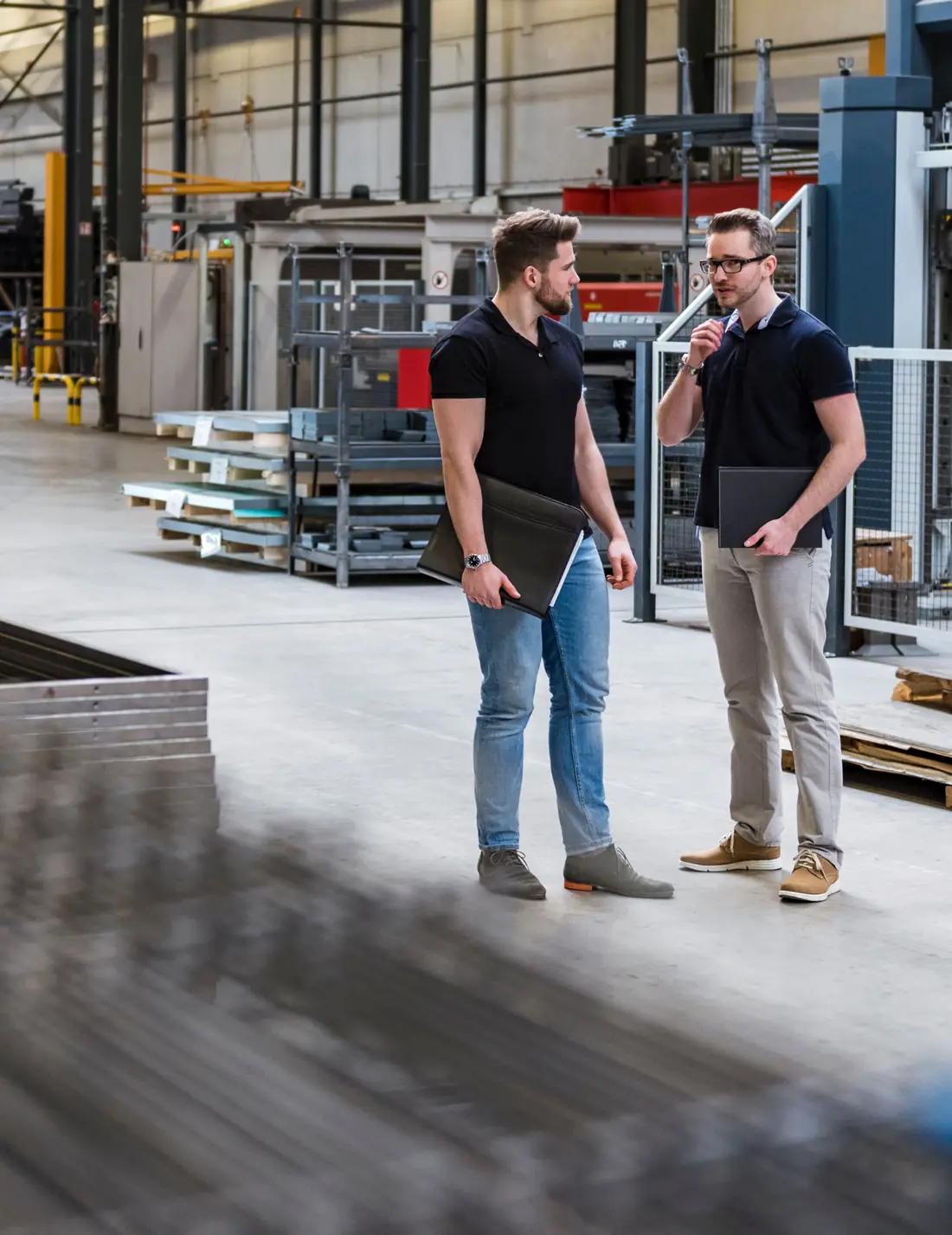Two colleagues talking on a factory floor, one holding a laptop