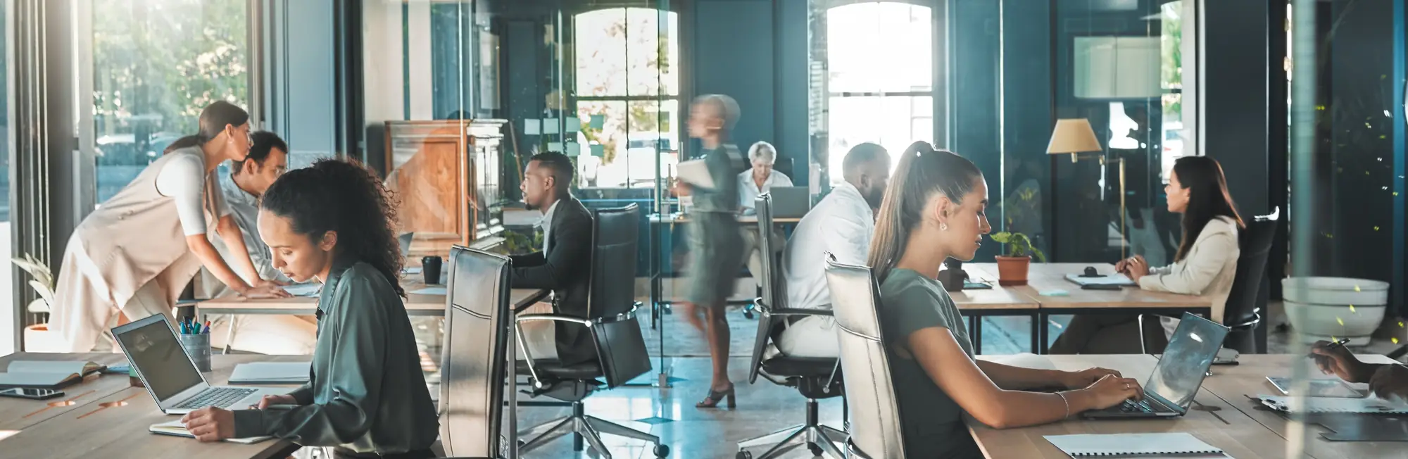 A busy open-plan office with people working at long shared desks
