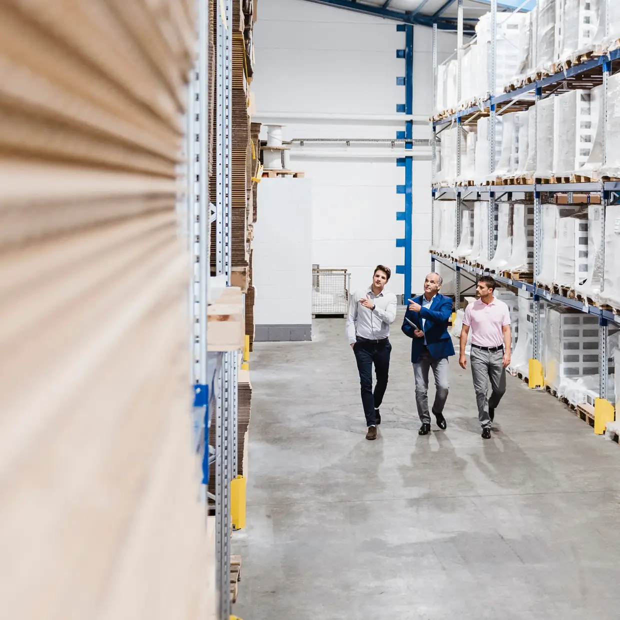 Three people walking and talking down a warehouse aisle lined with stocked shelving