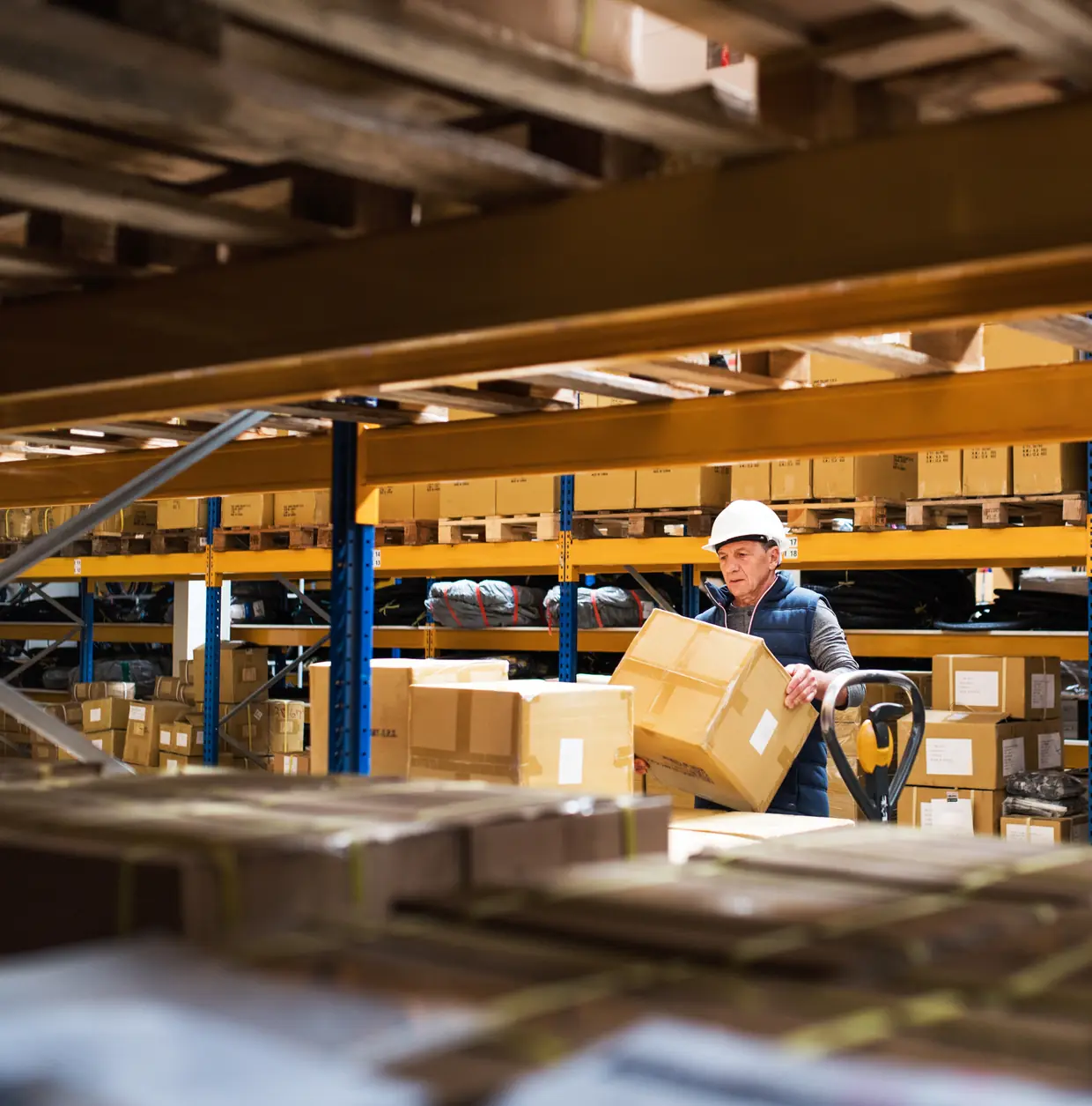 A warehouse worker in a hard hat lifting boxes from shelving